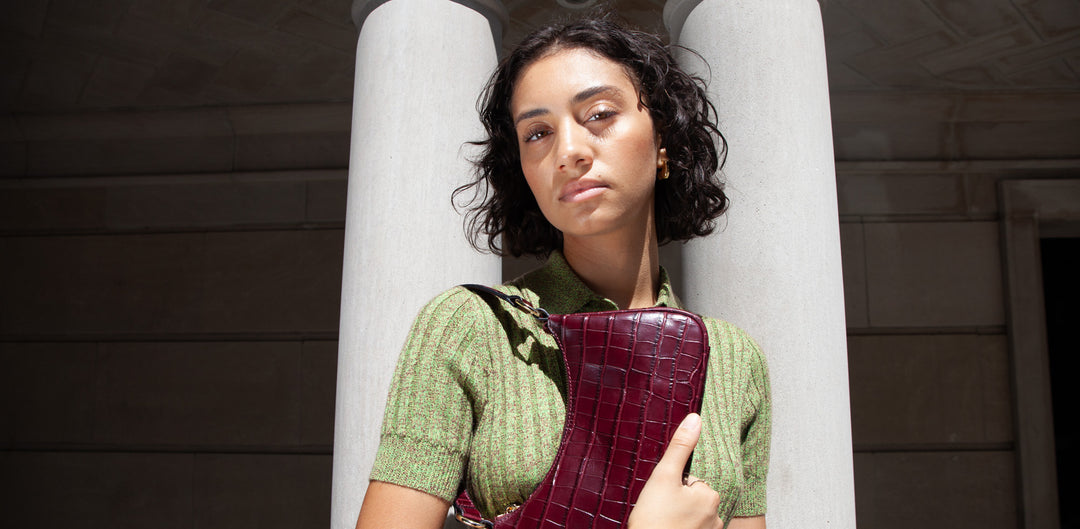 A woman standing in front of 2 white columns clutching a burgundy croc purse