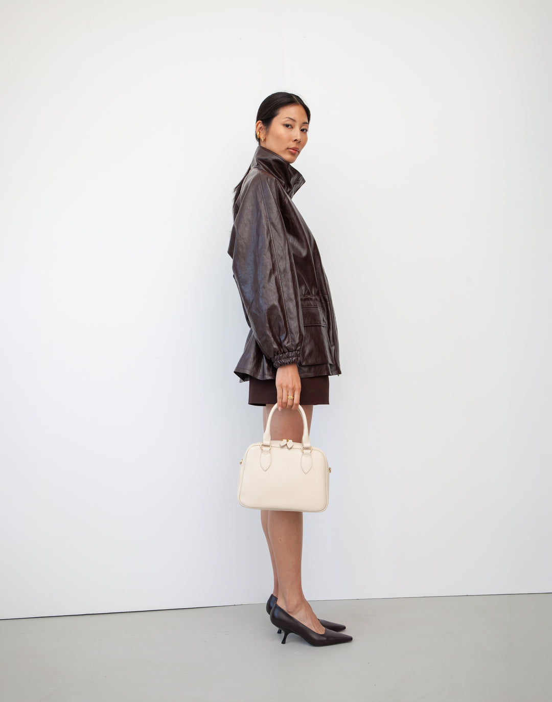 a model holds a hyer goods la corsa off-white leather bowling bag bone with gold hardware #color_bone