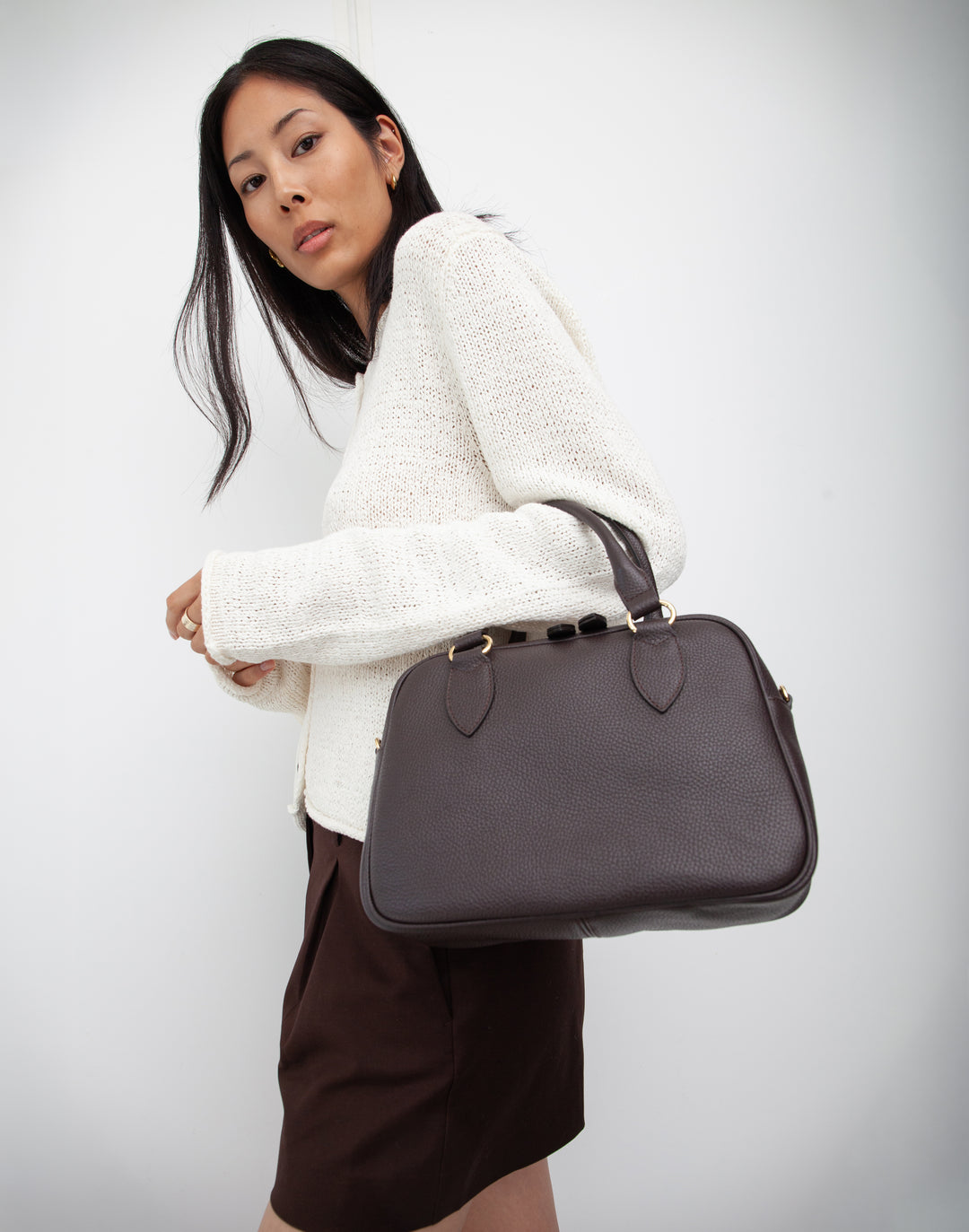 hyer goods la corsa dark brown leather bowling bag front view dark chocolate with gold hardware on models arm #color_dark-chocolate
