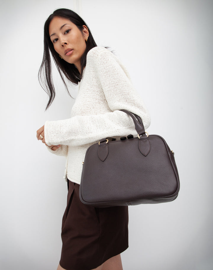 hyer goods la corsa dark brown leather bowling bag front view dark chocolate with gold hardware on models arm #color_dark-chocolate