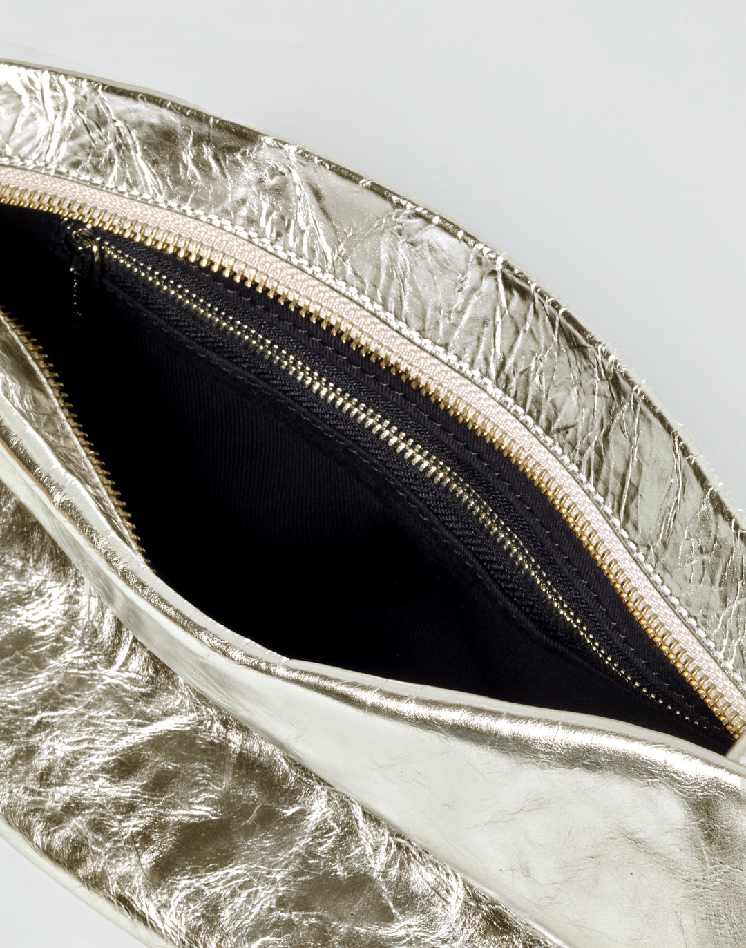inside view of a gold zipper and black lining inside a gold leather bag #color_gold
