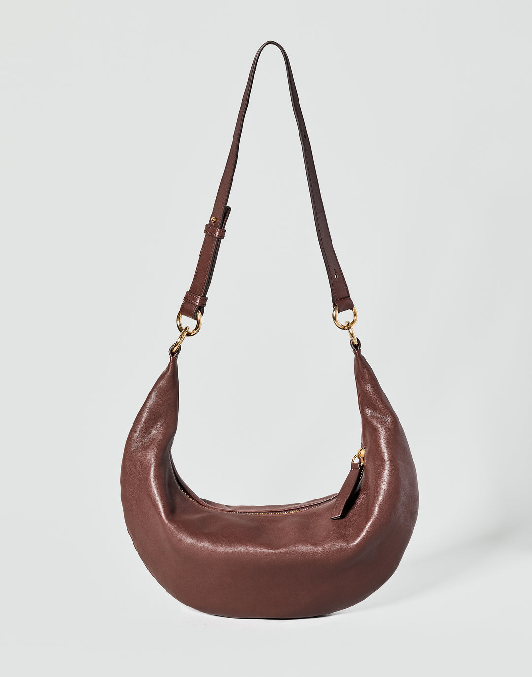 A dark brown leather crescent-shaped shoulder bag with a long strap and gold-tone hardware, shown against a light gray background. #color_bordeaux-vintage