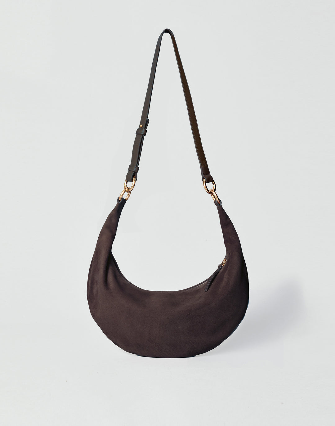 A dark brown HYER GOODS Piccola Ring Bag crescent-shaped shoulder bag made of suede, featuring a single adjustable shoulder strap with gold-tone hardware, set against a light gray background #color_chocolate-suede