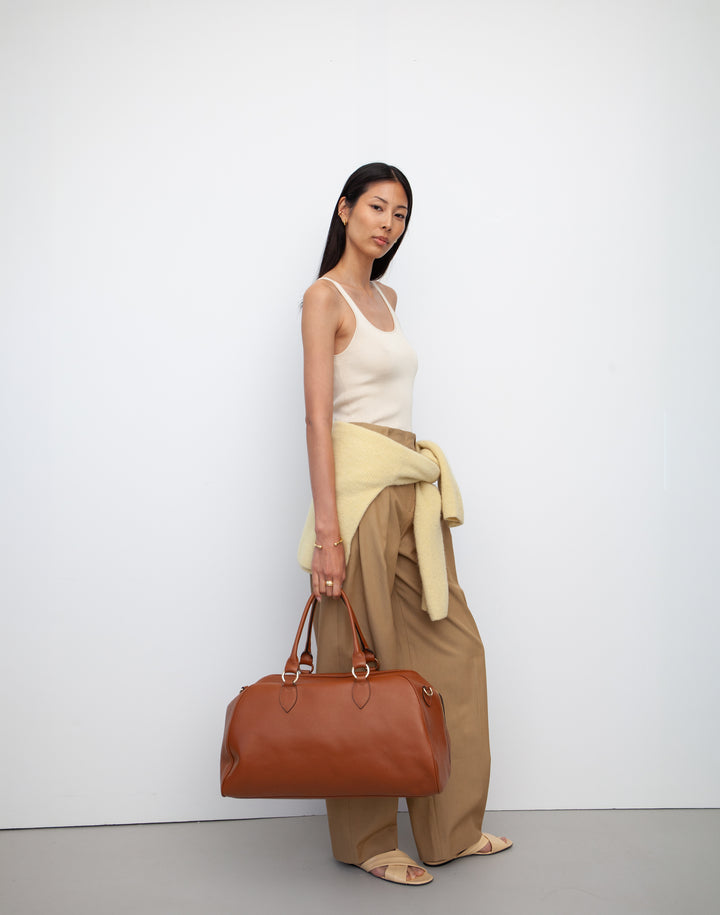 HYER GOODS tan leather la via weekender duffel bag held by model #color_cognac