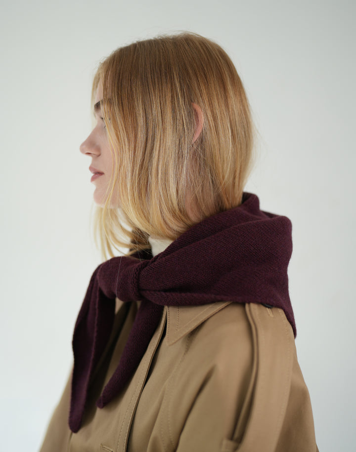 a cropped photo of a woman with blond hair wearing a burgundy scarf around her neck over a trench coat against a grey background #color_bordeaux
